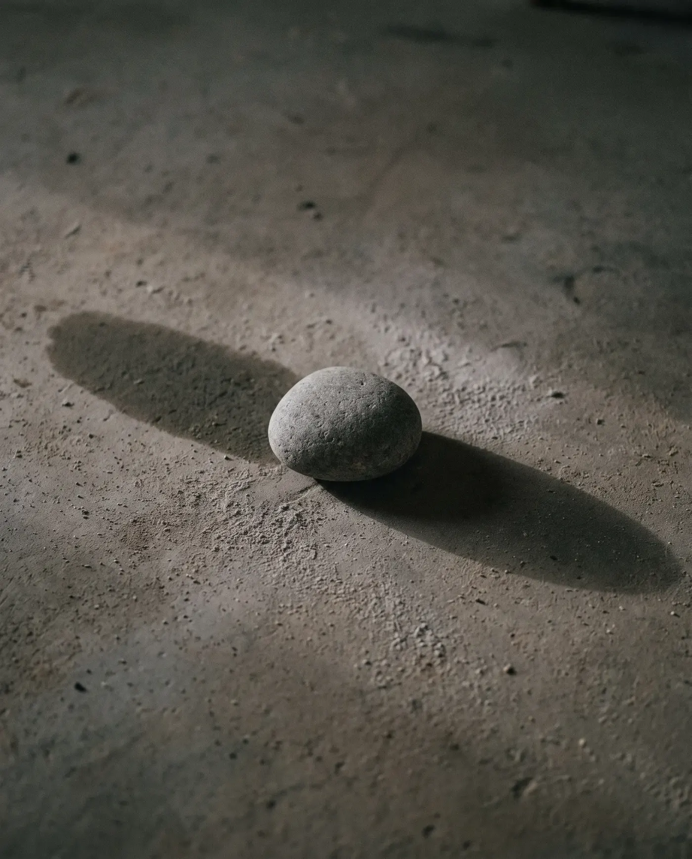 콘크리트 바닥에 놓인 조약돌 하나가 서로 다른 방향의 빛을 받아 길이가 크게 다른 두 그림자를 드리운 모습